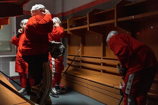 Hockey players in red uniforms preparing their gear in a locker room.